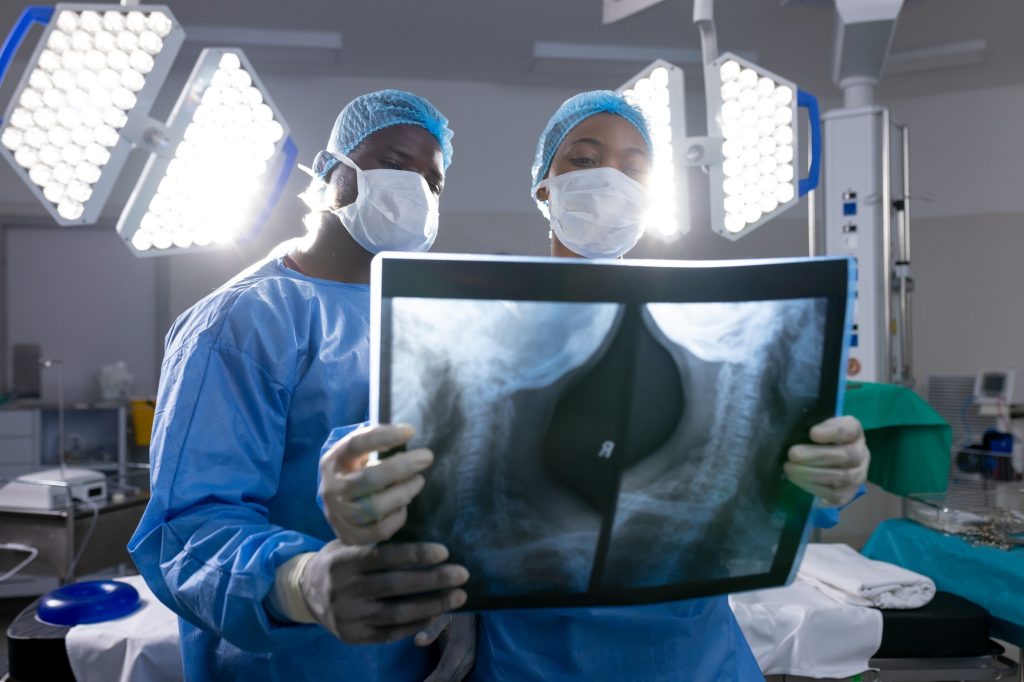 African american male and female doctors with face masks looking at x-rays in operating room