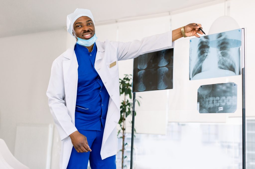 Young professional African-American man doctor in medical uniform and mask examining x-ray of